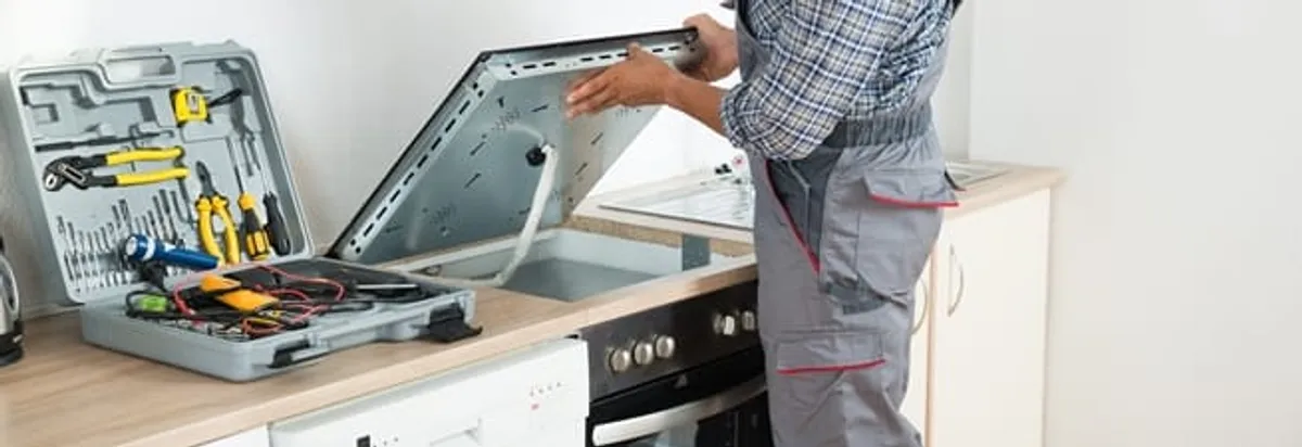 Cooktop repair technician lifting a built-in stovetop for service in Charleston, SC